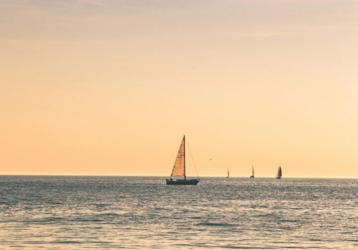 A sailboat is sailing in the ocean at sunset.